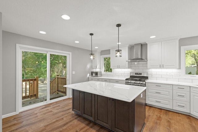 kitchen featuring a kitchen island, wall chimney range hood, white cabinetry, appliances with stainless steel finishes, and light wood-type flooring