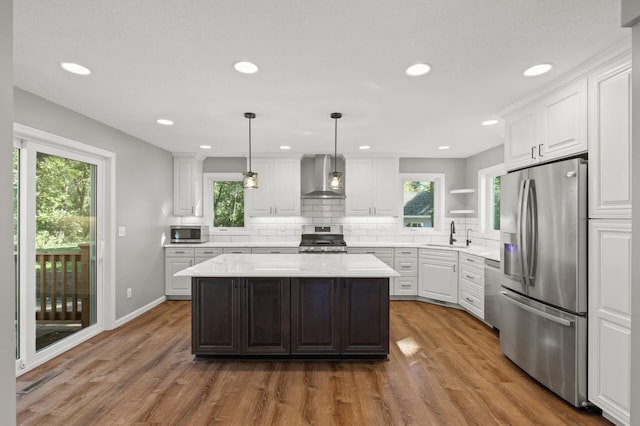 kitchen featuring wall chimney exhaust hood, a kitchen island, hardwood / wood-style floors, and stainless steel appliances