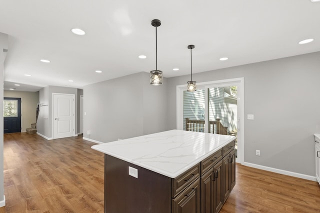 kitchen with dark brown cabinets, decorative light fixtures, a center island, and light hardwood / wood-style flooring