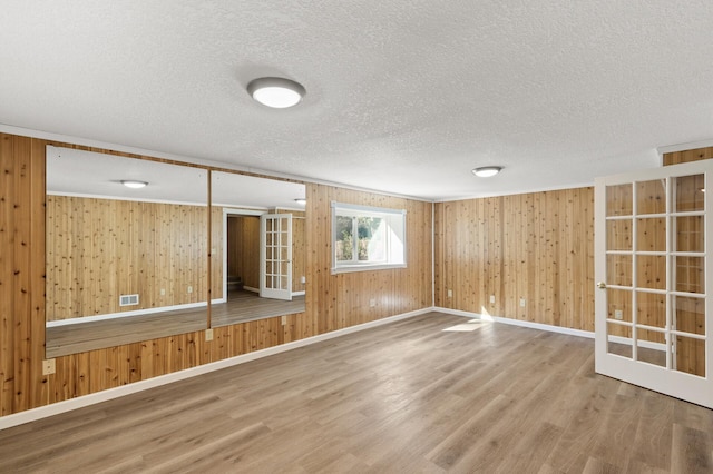 empty room with wooden walls, a textured ceiling, and hardwood / wood-style flooring