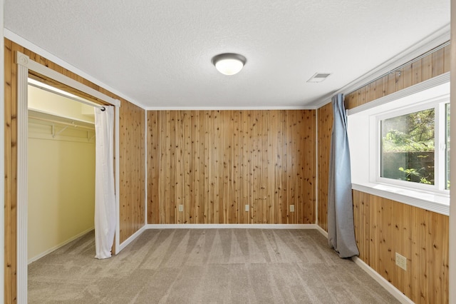 unfurnished bedroom featuring light colored carpet, a closet, wood walls, and ornamental molding