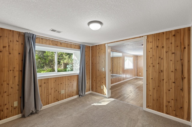 carpeted spare room featuring wooden walls and a textured ceiling