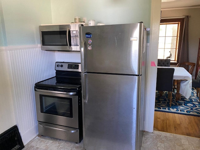 kitchen featuring appliances with stainless steel finishes, wainscoting, and stone finish flooring