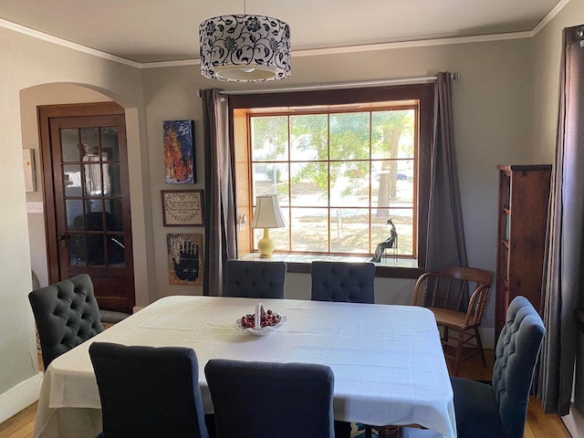 dining space with arched walkways, wood finished floors, baseboards, and ornamental molding
