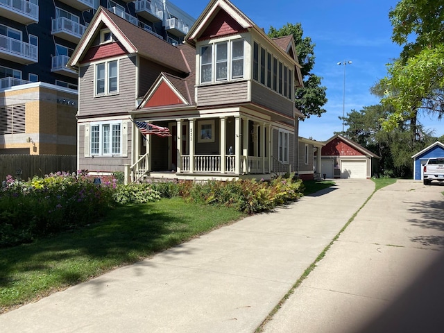 view of front of property with covered porch, a front yard, an outbuilding, and a garage