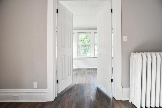 corridor with dark wood-type flooring and radiator heating unit