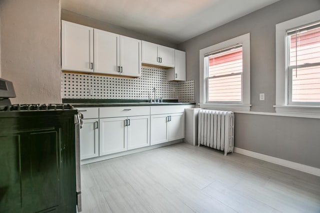 kitchen with black gas stove, white cabinetry, radiator, and plenty of natural light