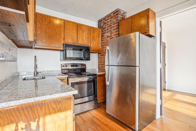 kitchen with light stone counters, appliances with stainless steel finishes, light hardwood / wood-style floors, and sink