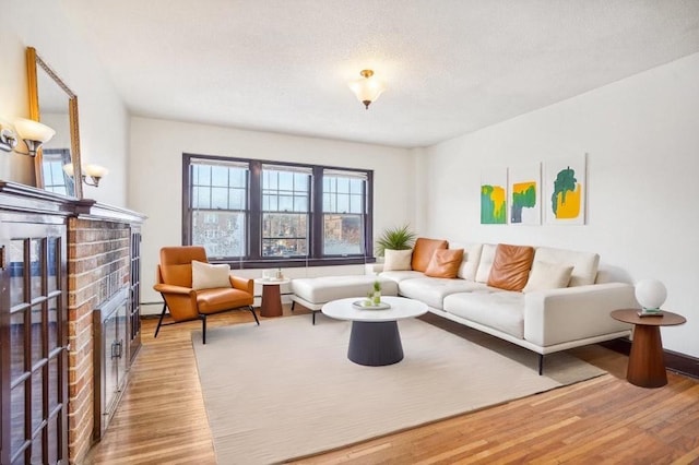 living room featuring a fireplace, a baseboard radiator, light hardwood / wood-style floors, and a textured ceiling