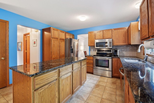 kitchen featuring light tile patterned floors, appliances with stainless steel finishes, a kitchen island, dark stone counters, and sink