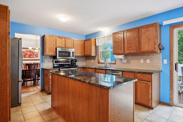 kitchen with sink, dark stone countertops, stainless steel appliances, a kitchen island, and decorative backsplash