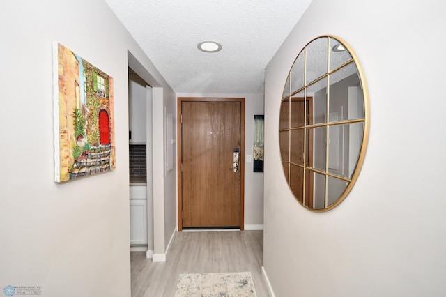 doorway to outside with a textured ceiling and light hardwood / wood-style floors