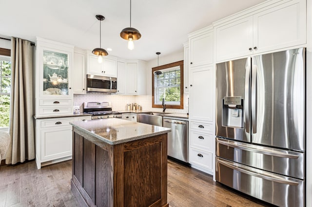 kitchen with dark wood-style flooring, backsplash, appliances with stainless steel finishes, a kitchen island, and a sink