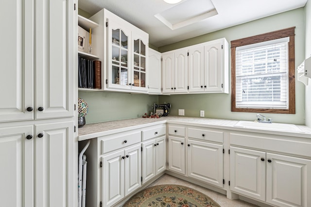 kitchen with glass insert cabinets, light countertops, white cabinets, and a sink