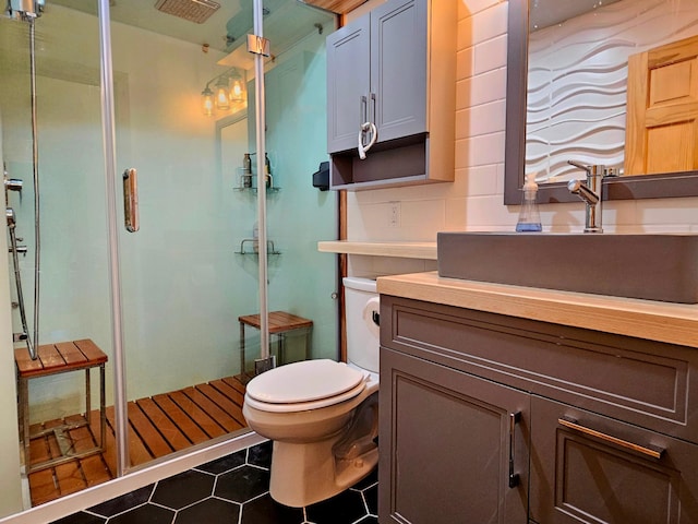 bathroom featuring tile patterned flooring, toilet, decorative backsplash, a shower with door, and vanity