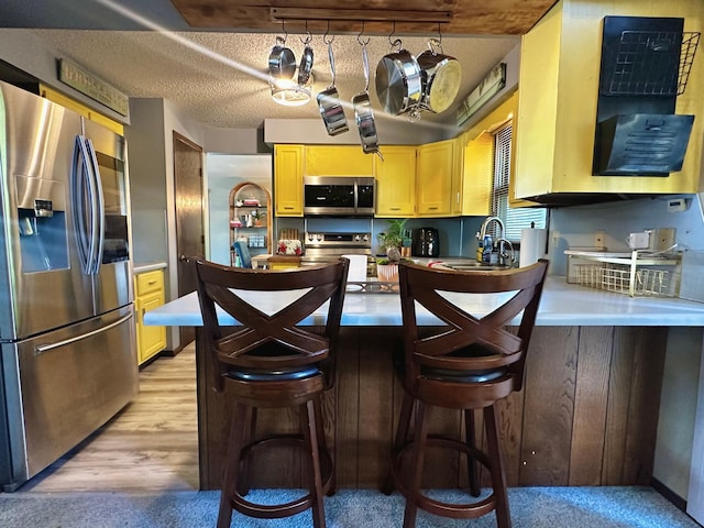 kitchen with a breakfast bar area, a textured ceiling, light wood-type flooring, sink, and stainless steel appliances