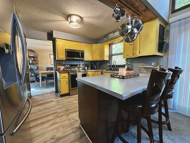 kitchen featuring sink, light brown cabinetry, appliances with stainless steel finishes, a textured ceiling, and light hardwood / wood-style floors