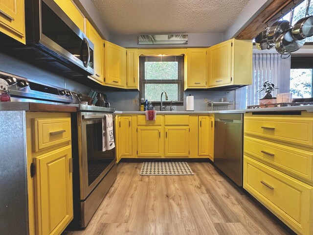 kitchen featuring appliances with stainless steel finishes, a textured ceiling, sink, and light hardwood / wood-style floors