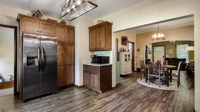 kitchen with arched walkways, brown cabinetry, dark wood-style flooring, and stainless steel fridge with ice dispenser