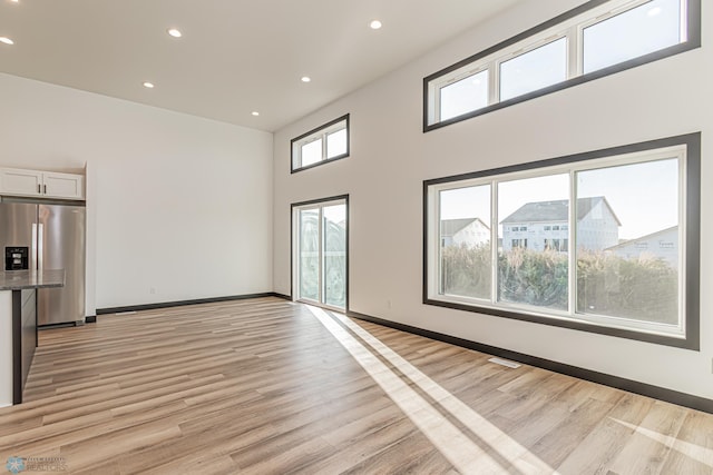 unfurnished living room with a high ceiling, light hardwood / wood-style floors, and a healthy amount of sunlight