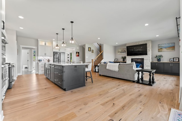 kitchen with light hardwood / wood-style floors, white cabinets, hanging light fixtures, a center island with sink, and a stone fireplace