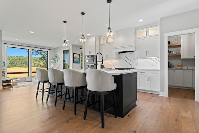 kitchen featuring light hardwood / wood-style flooring, white cabinetry, a center island with sink, and hanging light fixtures