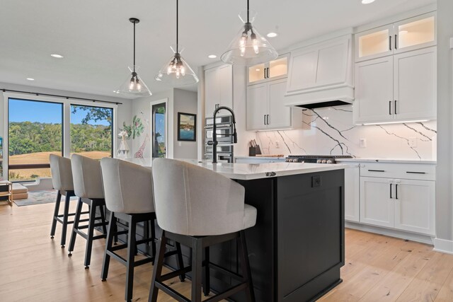 kitchen featuring an island with sink, white cabinets, pendant lighting, and light hardwood / wood-style flooring