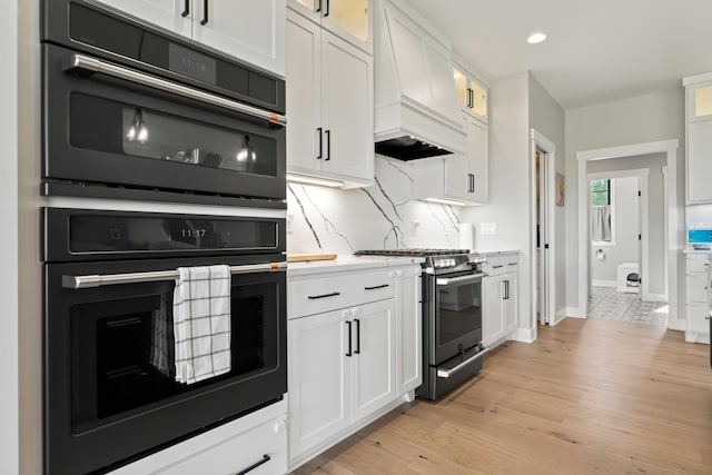 kitchen with light hardwood / wood-style flooring, stainless steel gas range, white cabinetry, and double oven