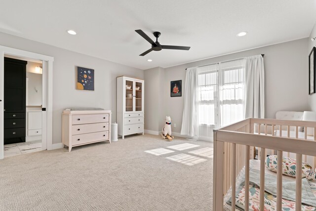 bedroom featuring light colored carpet, ceiling fan, and a nursery area