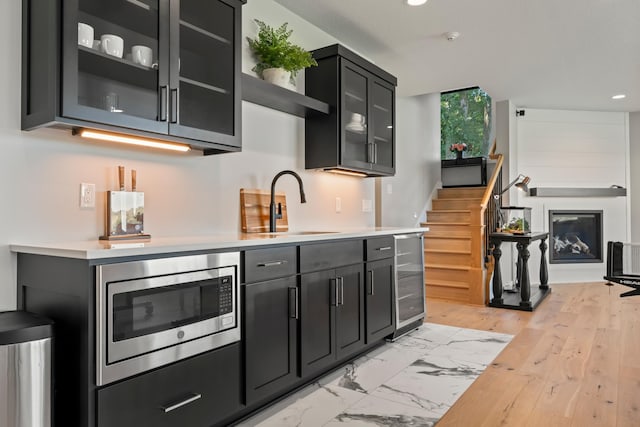 kitchen featuring light hardwood / wood-style floors, stainless steel microwave, beverage cooler, and sink