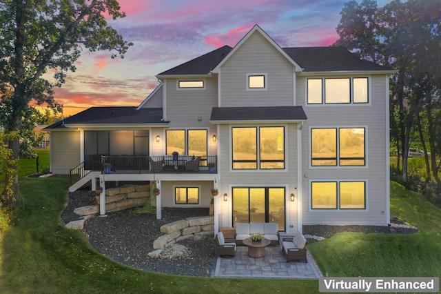 back house at dusk featuring a patio and a lawn