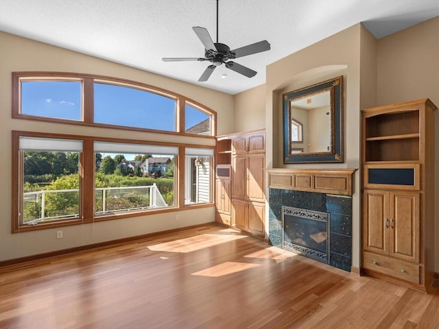 unfurnished living room with light hardwood / wood-style flooring, ceiling fan, a tile fireplace, and a textured ceiling