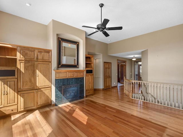 unfurnished living room with a tile fireplace, light hardwood / wood-style floors, and ceiling fan