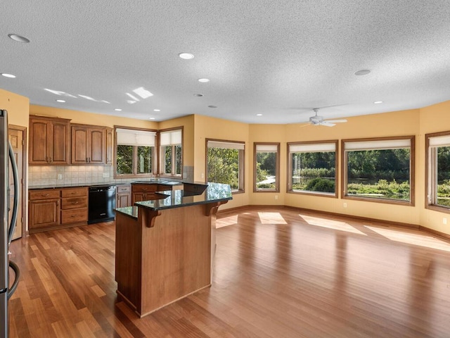 kitchen with a breakfast bar, black dishwasher, light hardwood / wood-style floors, a textured ceiling, and ceiling fan