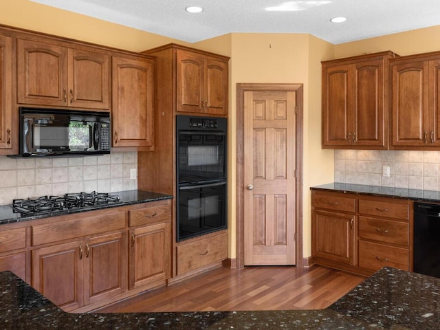 kitchen featuring decorative backsplash, black appliances, dark wood-type flooring, and dark stone counters