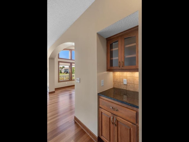 bar with a textured ceiling, light wood-type flooring, dark stone counters, and decorative backsplash