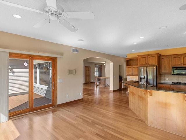 kitchen with dark stone counters, light hardwood / wood-style floors, tasteful backsplash, stainless steel appliances, and ceiling fan