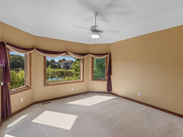 carpeted empty room with ceiling fan and a wealth of natural light