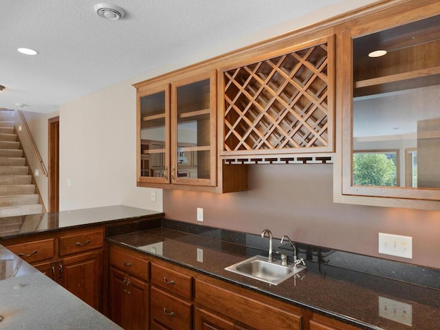 kitchen with a textured ceiling, dark stone counters, and sink