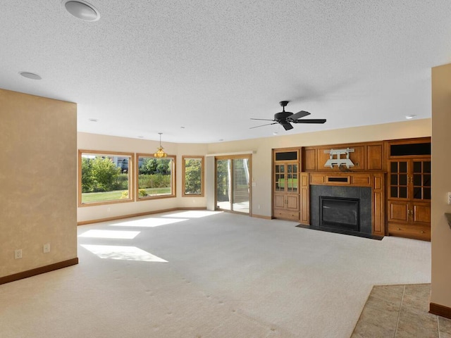 unfurnished living room with a textured ceiling, a tiled fireplace, ceiling fan, and light colored carpet