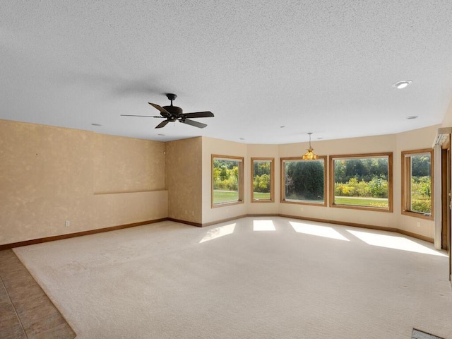 unfurnished room featuring a textured ceiling, carpet flooring, ceiling fan, and plenty of natural light