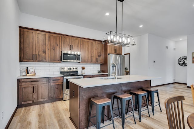 kitchen featuring hanging light fixtures, a kitchen island with sink, stainless steel appliances, an inviting chandelier, and light wood-type flooring