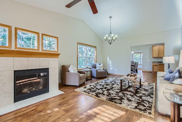 living room with light wood-type flooring, ceiling fan with notable chandelier, a fireplace, and vaulted ceiling