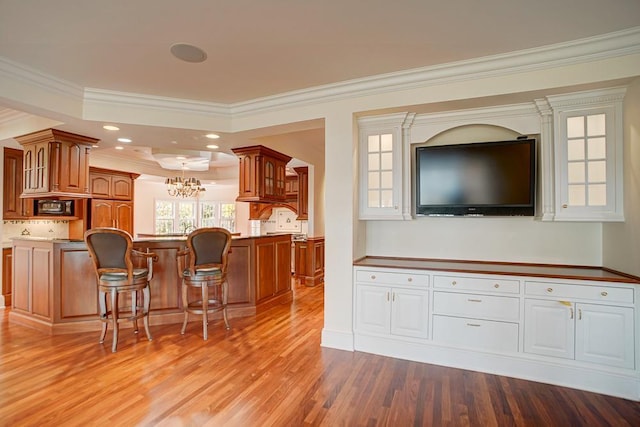 kitchen featuring a center island, light hardwood / wood-style flooring, ornamental molding, a kitchen bar, and black microwave