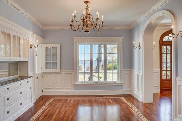 unfurnished dining area featuring a healthy amount of sunlight, crown molding, dark wood-type flooring, and a chandelier