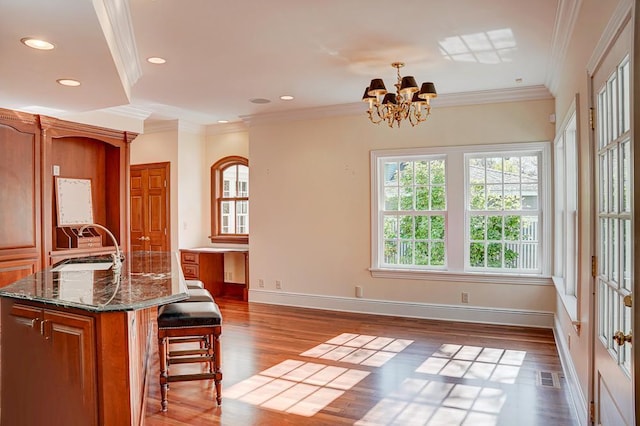 kitchen with an island with sink, a chandelier, wood-type flooring, a breakfast bar, and ornamental molding