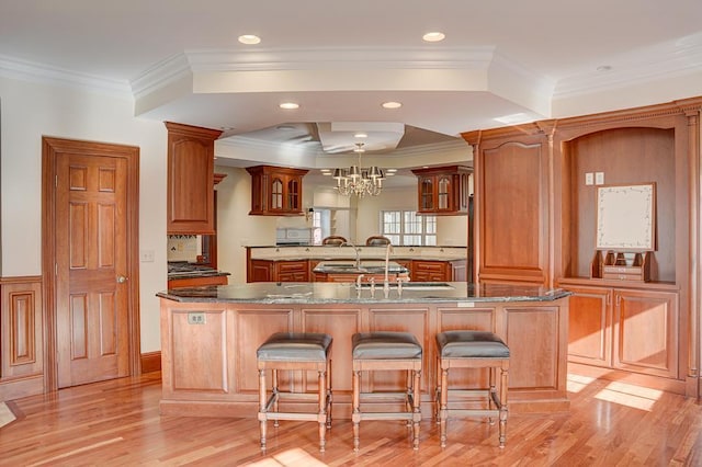 kitchen with a kitchen bar, crown molding, an island with sink, and light wood-type flooring