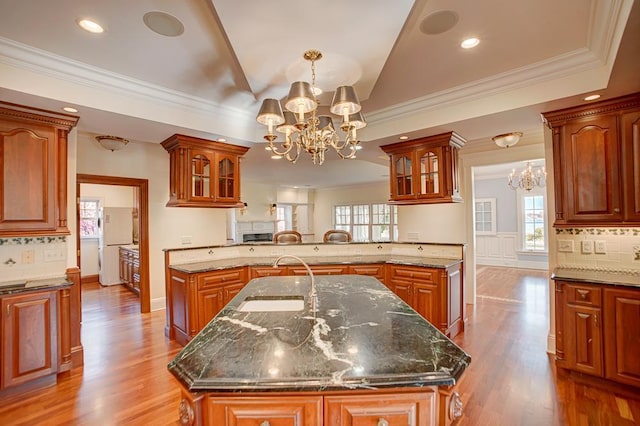 kitchen featuring dark stone countertops, an island with sink, light hardwood / wood-style floors, and a notable chandelier