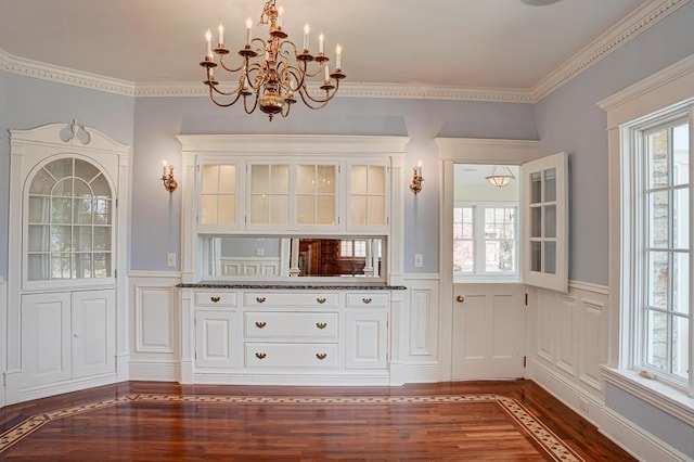 unfurnished dining area featuring dark hardwood / wood-style flooring, a healthy amount of sunlight, a notable chandelier, and ornamental molding