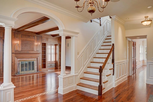 staircase with hardwood / wood-style floors, an inviting chandelier, crown molding, and a brick fireplace